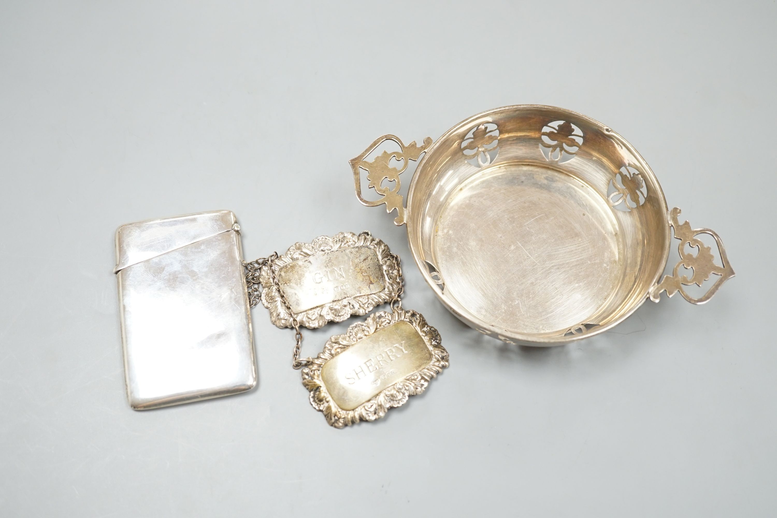 A circular sweetmeat with pierced sides and lug handles, Birmingham 1954, 10.75cm diameter, a plain rectangular card case, Birmingham 1914 and two modern silver wine labels, Gin & Sherry.